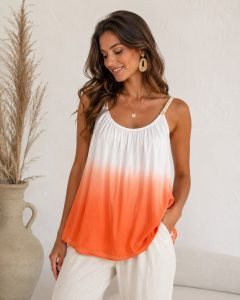 Eine lächelnde Frau trägt das „Sunny Ombre“-Oberteil – es besticht durch sanfte Ombré-Farbtöne, eine lockere Passform und ist sowohl für die Arbeit als auch für die Freizeit vielseitig einsetzbar; dazu trägt sie eine cremefarbene Hose.