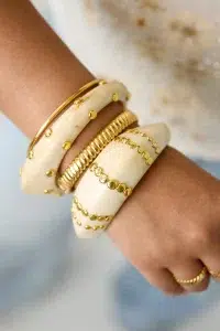 Nahaufnahme von drei cremefarbenen, klobigen Armreifen mit goldenen Punkten, einem goldenen Armband und einem Ring – ein trendiges Set zum Kombinieren für elegante Alltagsmode.