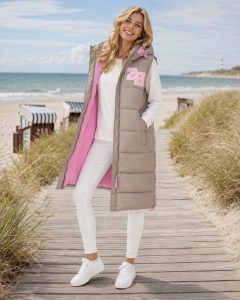 Eine Frau auf der Strandpromenade präsentiert die XXL Lange Steppweste „ZH Patch“ – eine ultrawarme, stilvolle und winddichte Weste, die sich perfekt für Ausflüge an die Küste eignet.