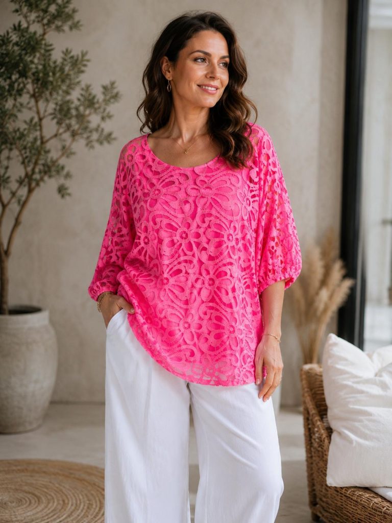 Eine Frau präsentiert ein leuchtend pinkes Oberteil mit Blumenmuster und eine weiße Hose mit weitem Bein – aus atmungsaktivem Stoff, mit figurschmeichelnder Passform; perfekt für einen lässigen Sommerlook.